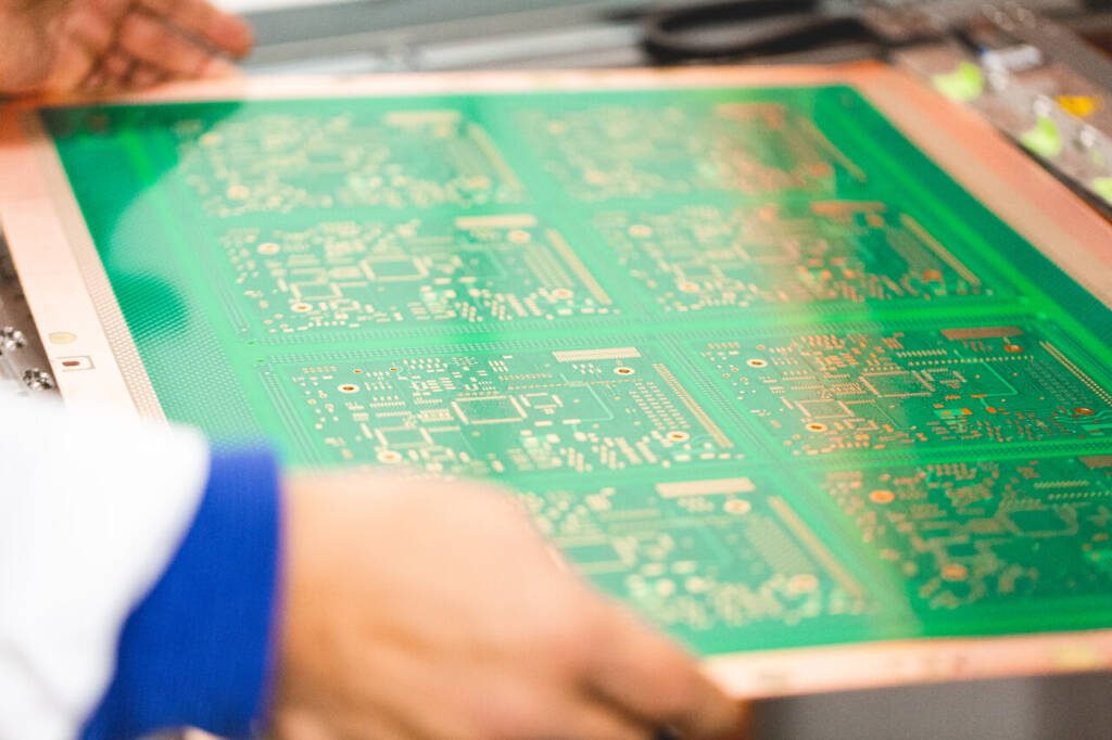 close up shot of a person in a white labcoat with blue sleeves underneath picking up a green circuit board